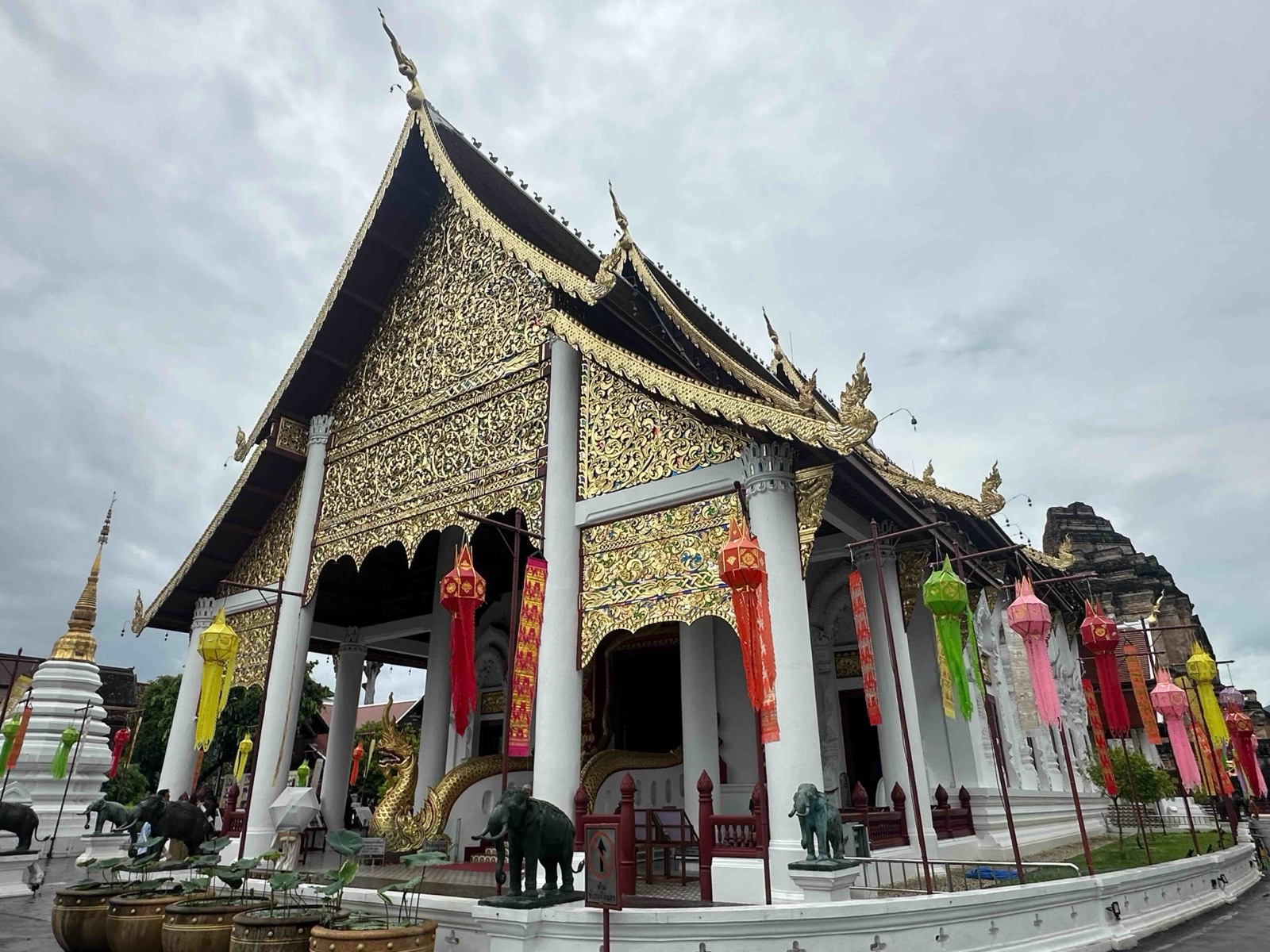 A temple hall at Wat Chedi Luang in Chiang Mai under a cloudy sky, with colourful lanterns hanging between the columns